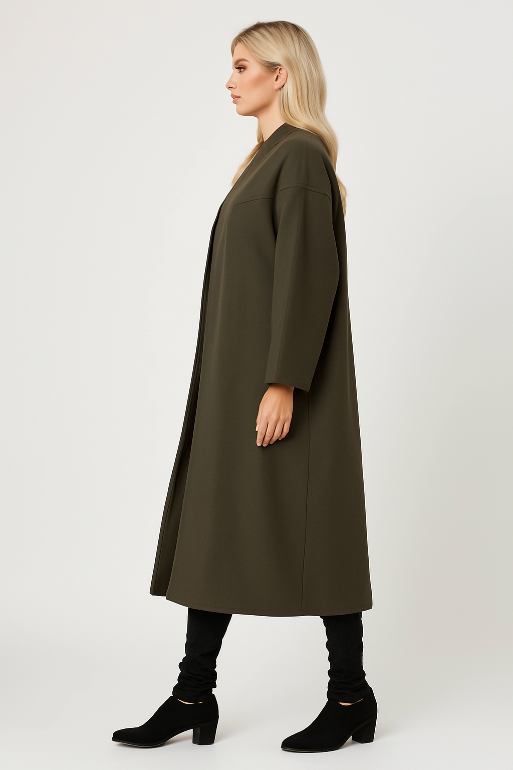Woman wearing olive green Charlie Long Coat with longline design and side pockets, styled with black pants and boots, side profile view.