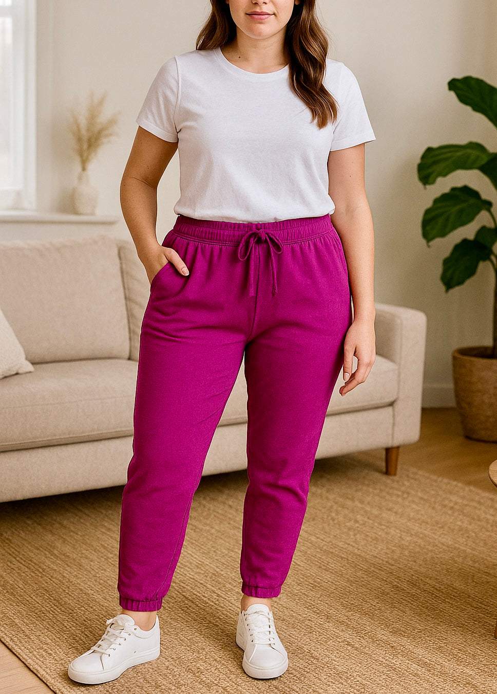 Woman wearing Megan Magic Trousers in vibrant purple with a white t-shirt and white sneakers in a cozy living room setting
