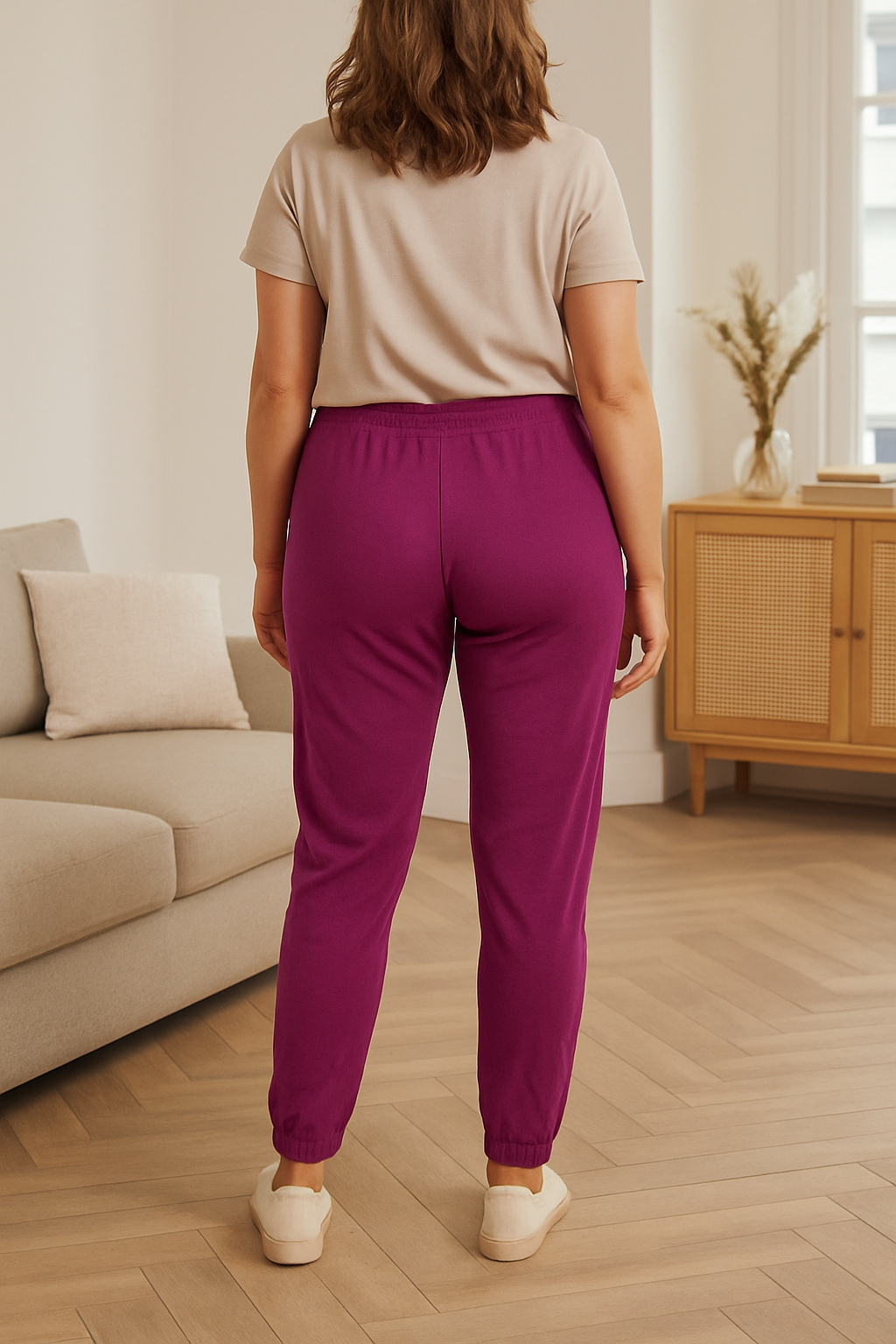 Woman wearing plum Megan Magic Trousers with a slim-leg fit and elasticated ankles viewed from the back in a modern living room