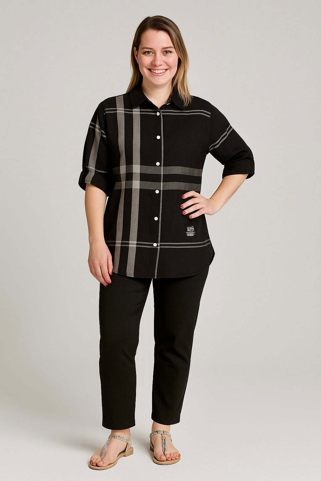 Woman wearing a black and gray plaid button-down shirt, standing and smiling against a plain background