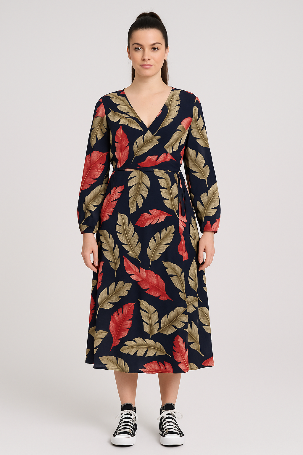 Woman wearing Jess Floral Wrap Dress with red and beige leaf print on navy background, long sleeves, V-neck, and tie waist, paired with black and white sneakers