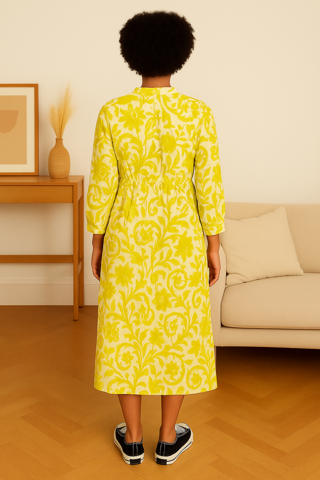 Back view of a woman wearing a yellow floral Italian Maxi Dress made of lightweight viscose in a cozy living room setting.